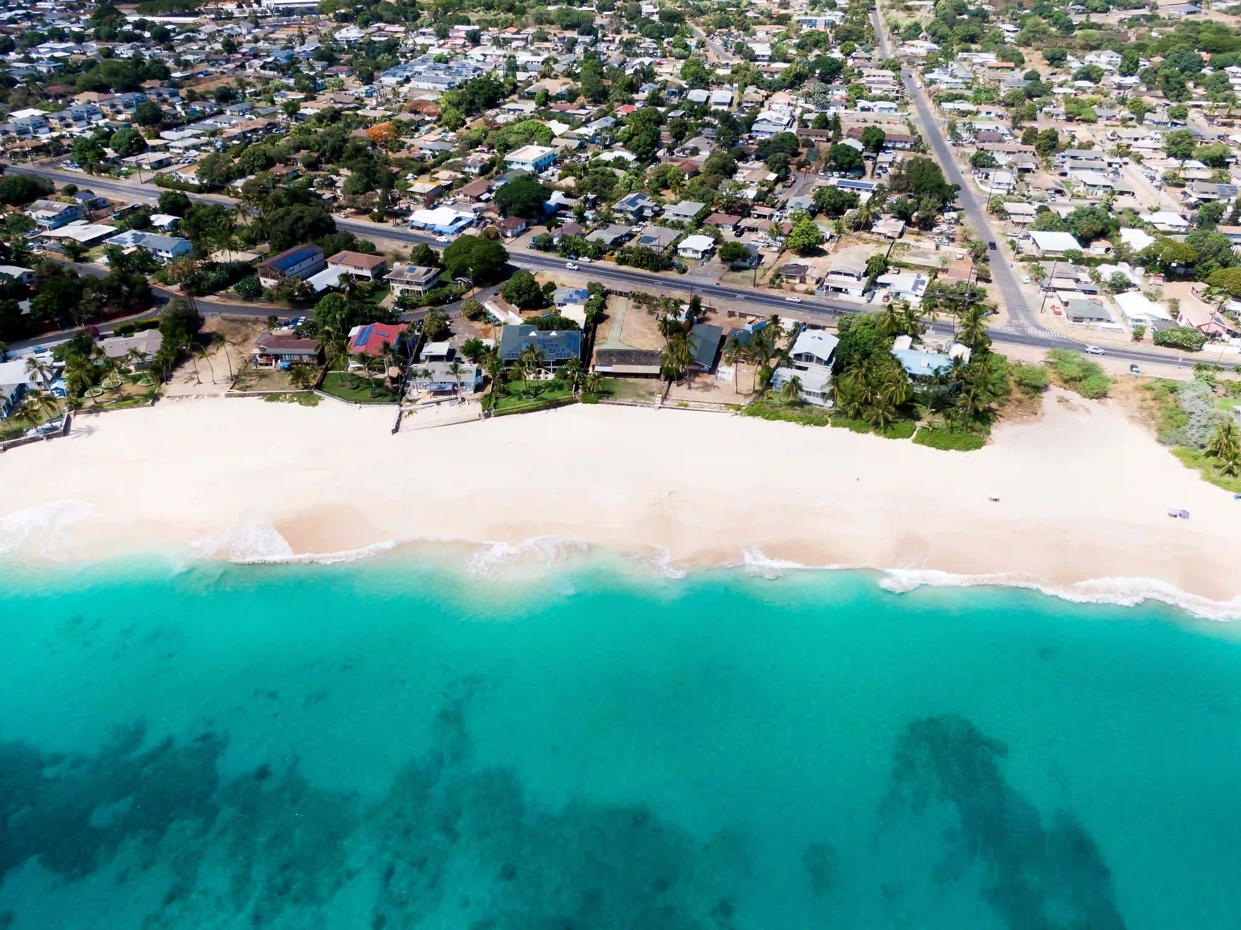 A west Oʻahu neighbourhood from the air, houses and palms meeting the sand and the reef beyond