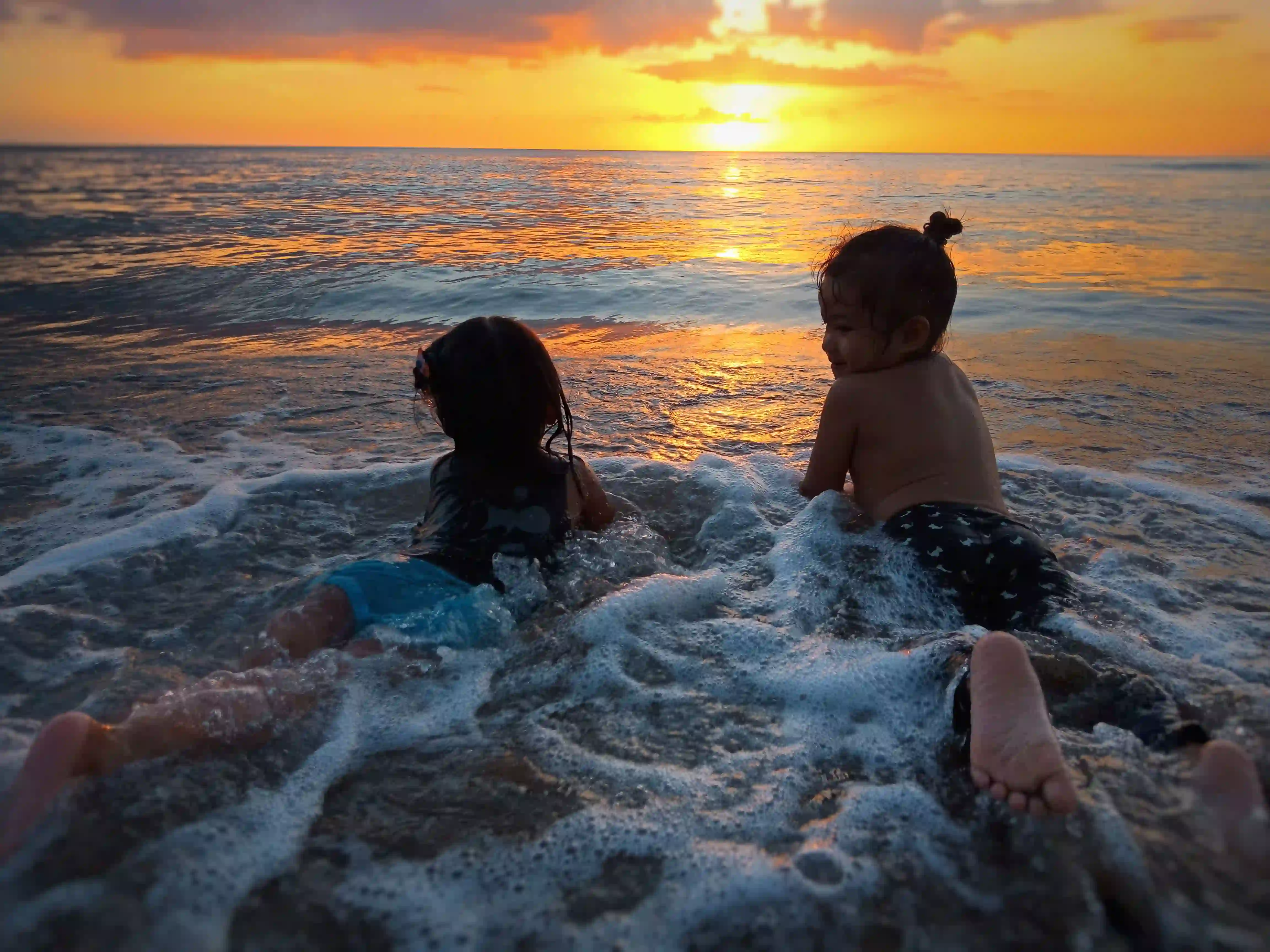 Two children sitting in the shorebreak at sunset