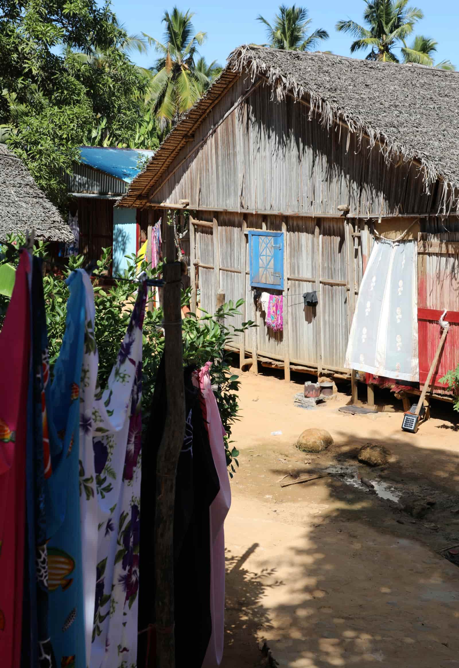 A thatched village home with laundry drying on the line and a small solar panel propped against the porch